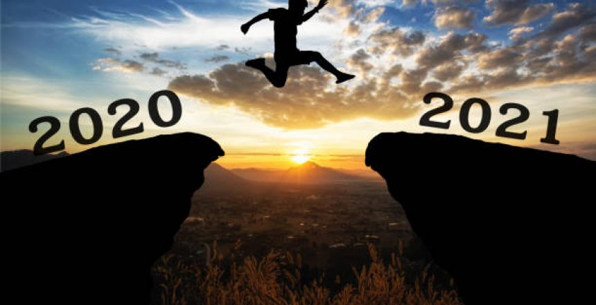 A young man jump between 2020 and 2021 years over the sun and through on the gap of hill  silhouette evening colorful sky. happy new year 2021.