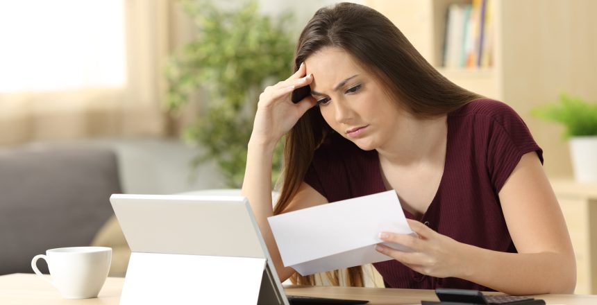 Worried woman calculating accountancy reading a letter sitting in a desk at home